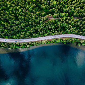 Aerial view of road between green summer forest and blue lake in Finland